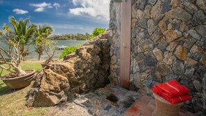 Ein Badezimmer mit Steinsäulen, einer Dusche, einem Blumentopf und Blick auf einen See.