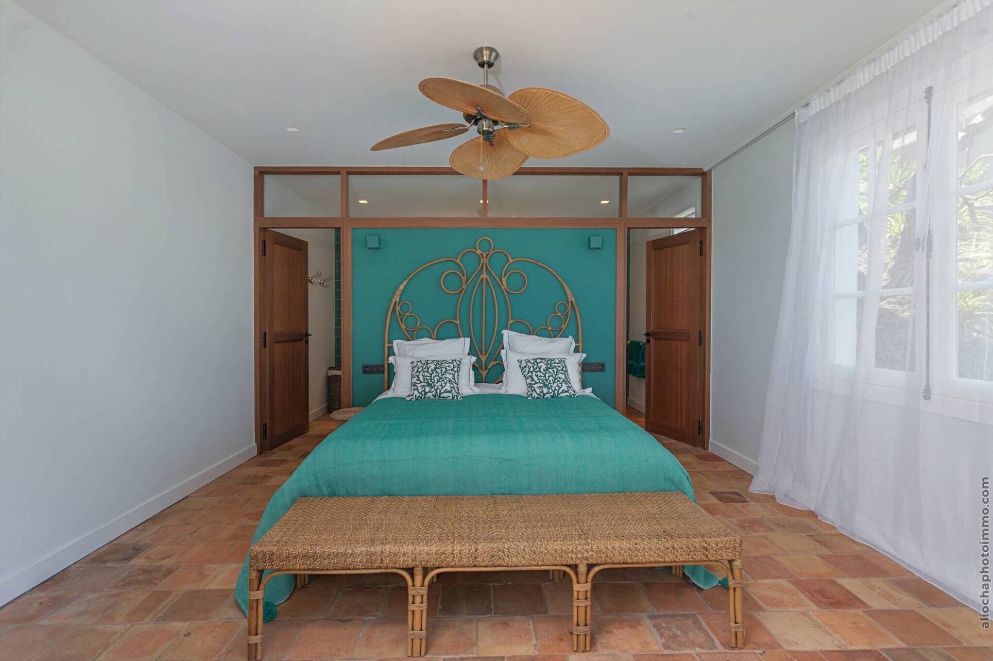 A bedroom with a bed, a ceiling fan, a window with curtains, and a wooden door.