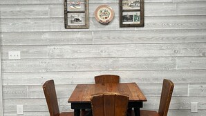 Un coin repas avec une table en bois et quatre chaises, adossé à un mur en bois gris orné de tableaux et d’assiettes décoratives.