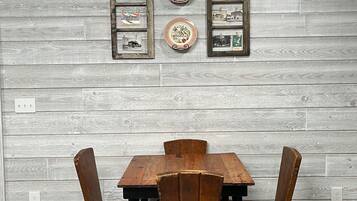 A dining area with a wooden table and four chairs, set against a grey wooden wall with framed pictures and plates.
