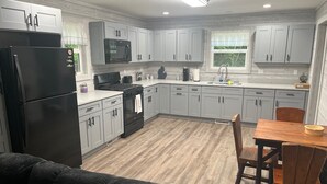 Une cuisine moderne avec des meubles gris, un réfrigérateur noir, une cuisinière et un coin repas comprenant une table et des chaises en bois.