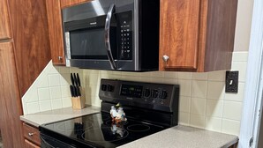 Una cocina con armarios de madera, un microondas negro, una estufa y un salpicadero de azulejos.