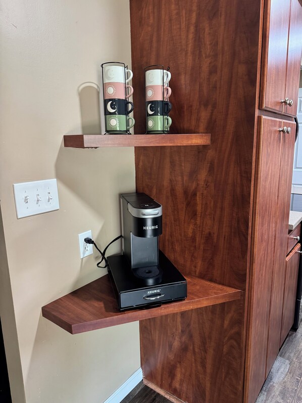 A kitchenette with a coffee maker on a shelf, a power outlet, and a cabinet.