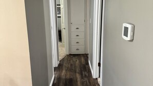Un estrecho pasillo con suelo de madera, paredes blancas y una puerta blanca al final.