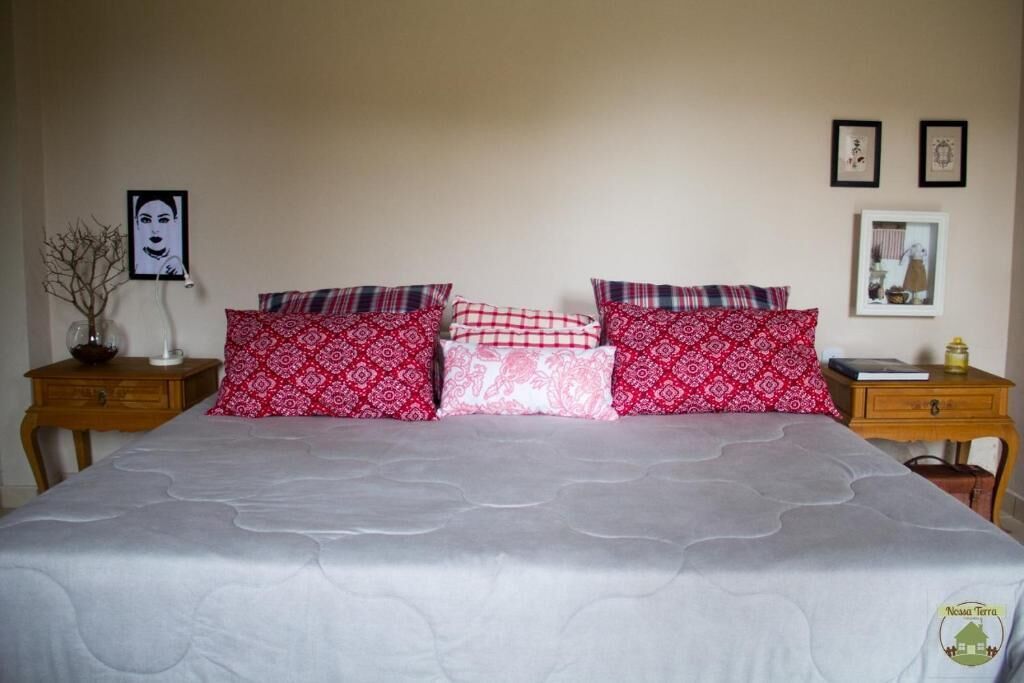 Ein Bett mit gemusterten Kissen, ein Nachttischchen mit Lampe und ein gerahmtes Bild an der Wand.