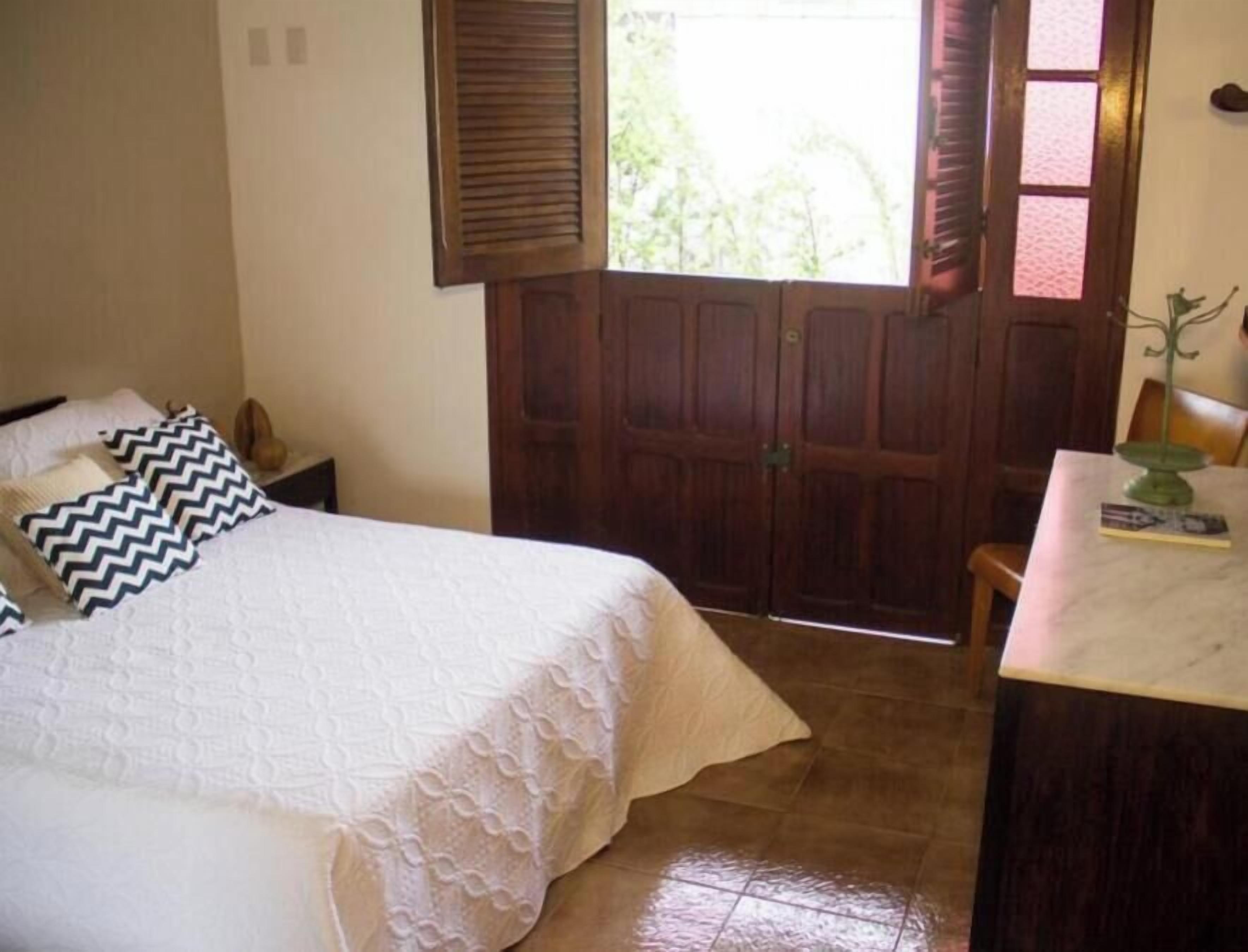 Un dormitorio con cama, mesita de noche, puerta de madera y una pequeña mesa con lámpara.