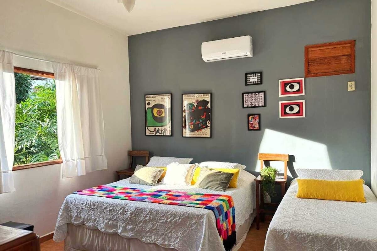 Un dormitorio con una cama, dos mesitas de noche, un ventanal con cortinas y decoración en la pared.