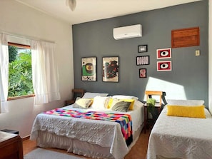 A bedroom with a bed, two bedside tables, a window with curtains, and wall art. - Pousada Nossa Terra (Rio Novo)