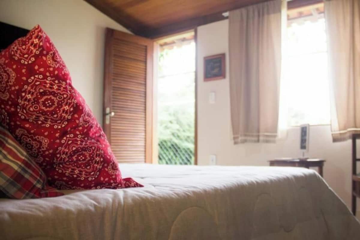 Un dormitorio con cama, una silla, un escritorio y una ventana con cortinas.