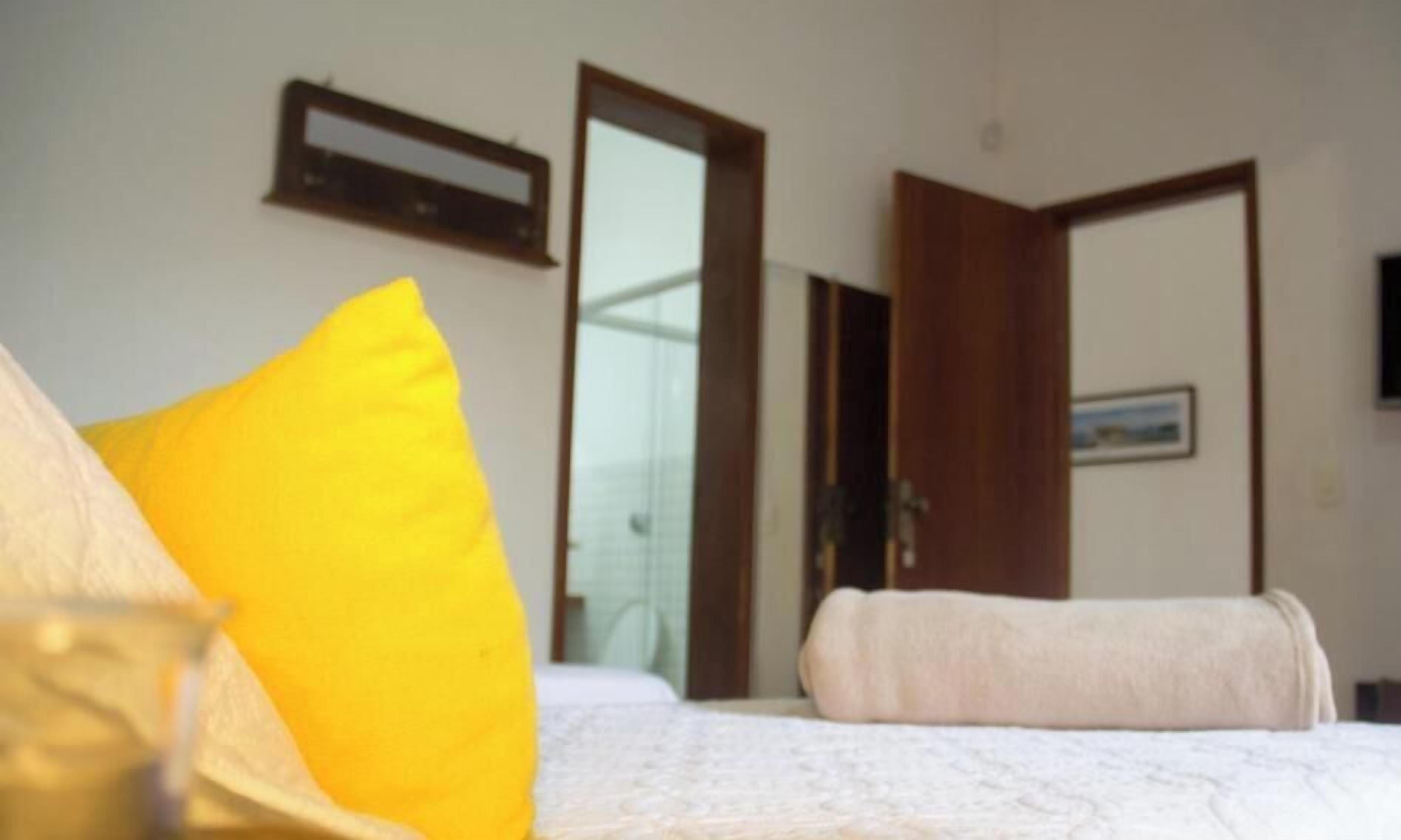 Quarto com cama, travesseiro amarelo, travesseiro branco e cabeceira de madeira.