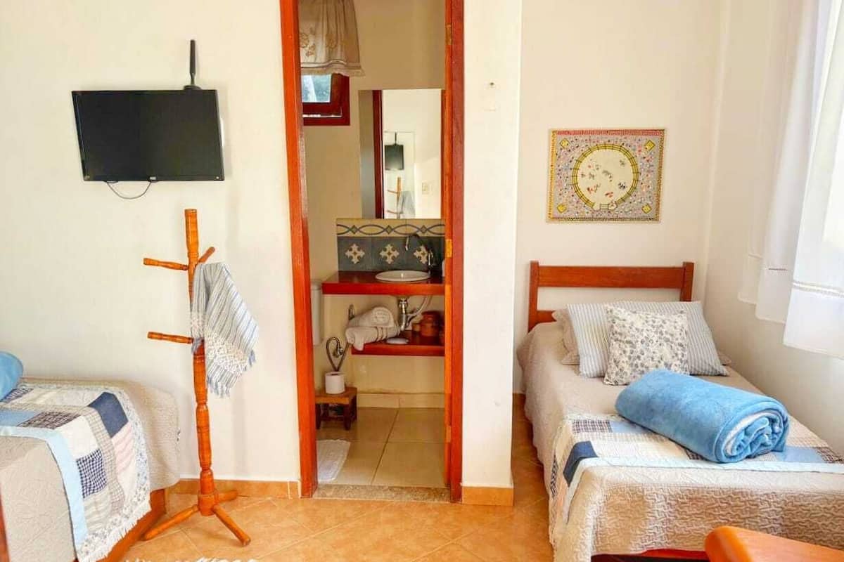 Un dormitorio con dos camas, un televisor, un espejo y un baño visible a través de una puerta abierta.