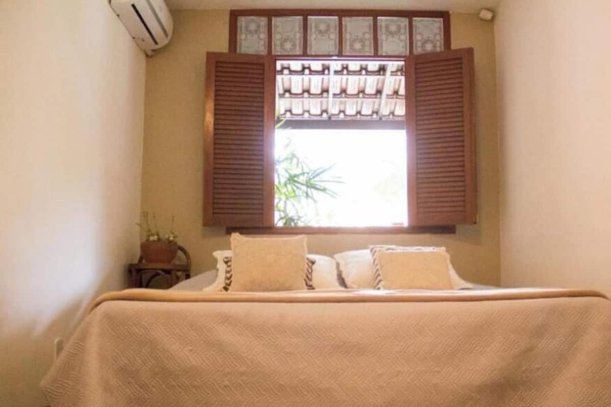 Un dormitorio con una cama, una ventana con contraventanas de madera, una mesita de noche y una planta en maceta.