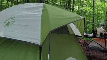 Een groene tent met een recyclinglogo, midden in een bos met bomen op de achtergrond.