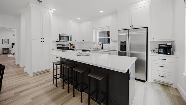 Una cocina moderna con armarios blancos, una isla grande con taburetes de bar, electrodomésticos de acero inoxidable y suelo de madera.