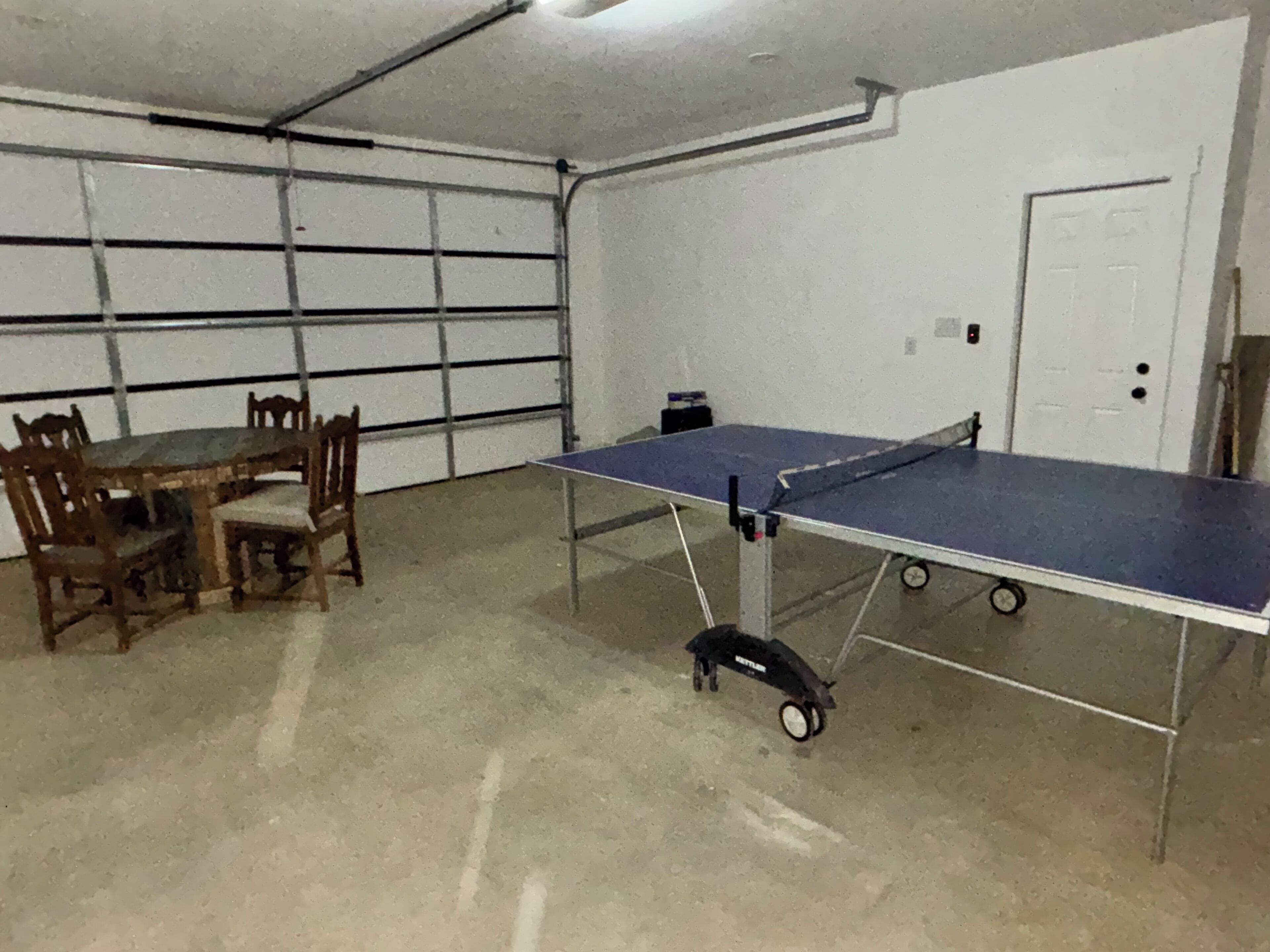 A room with a ping pong table, chairs, a table, and a door.