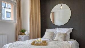 Una camera da letto con un letto grande, uno specchio tondo a parete, un comodino con una lampada e una finestra con tende.