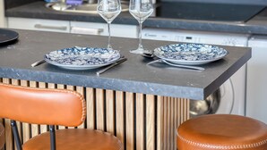 Un'area pranzo con due piatti bianchi e azzurri decorati, due bicchieri da vino e un coltello su un piano di lavoro scuro.