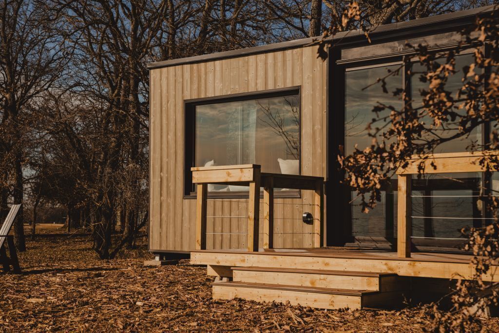 Una cabana de fusta moderna amb finestres grans, un balcó de fusta i una porta.