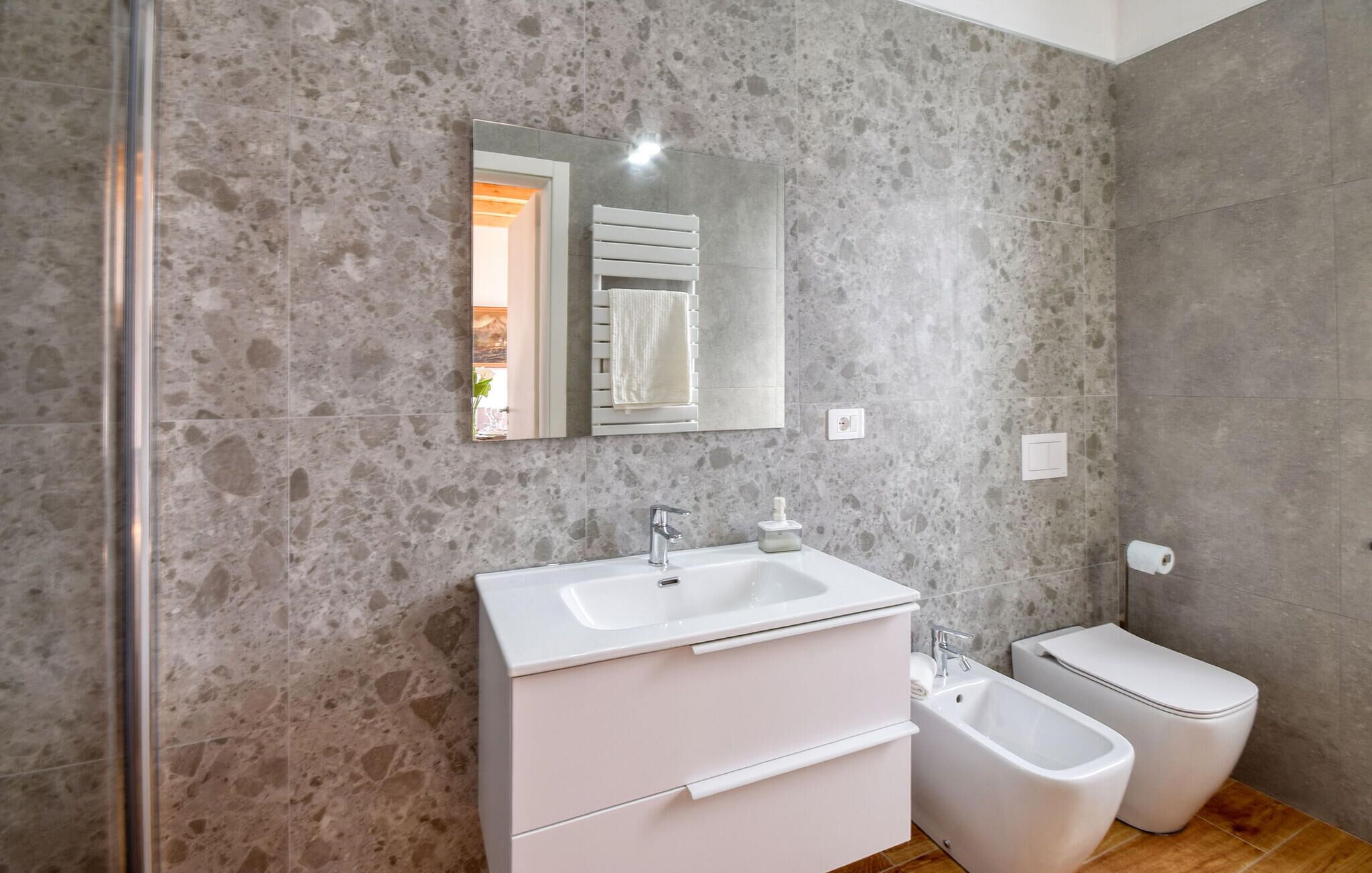 A modern bathroom with a stone wall, a white sink, a bidet, and a toilet.