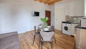 Una cocina moderna con lavadora integrada, un comedor con una mesa dispuesta para cuatro personas y un televisor montado en la pared.