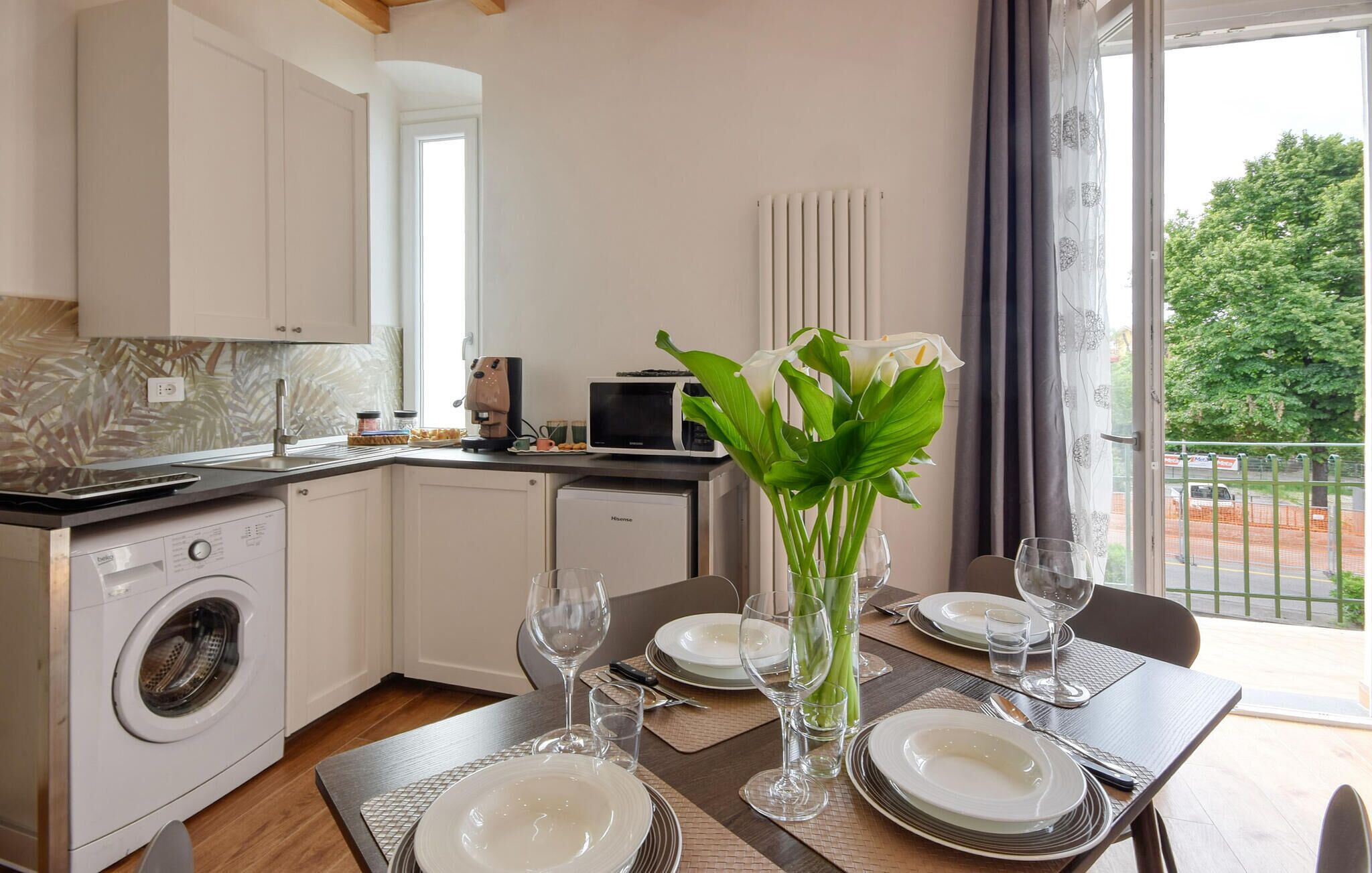 Una cocina moderna con lavadora y secadora integradas, un comedor con mesa dispuesta para cuatro, y vista al exterior.