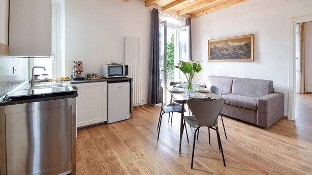 Una cocina moderna con lavavajillas integrado, un comedor con una mesa preparada para dos personas y una sala de estar con sofá y un cuadro en la pared.