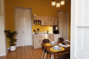 Une cuisine de taille réduite avec des meubles blancs, une table à manger agrémentée de sets de table jaunes et une plante en pot.