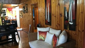 Interior acolhedor em madeira, com sofá, mesa de jantar e obras de arte.