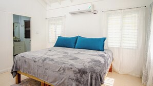 Ein Schlafzimmer mit einem Bett, einem Fenster mit Jalousien, einer Klimaanlage und einem Spiegel.
