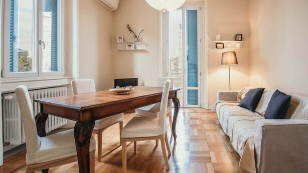A dining area with a wooden table and chairs, a sofa, and a lamp.