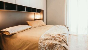 A bedroom with a bed, a headboard with built-in lighting, and a window with curtains.