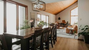 A spacious dining area with a wooden table and chairs, a hanging light fixture, and large windows allowing natural light. - LAKESIDE CITY GETAWAY (Roseville)