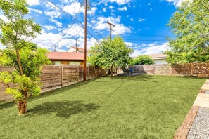 Un jardin avec une clôture en bois, une pelouse verdoyante et un espace patio aménagé avec du mobilier d’extérieur.