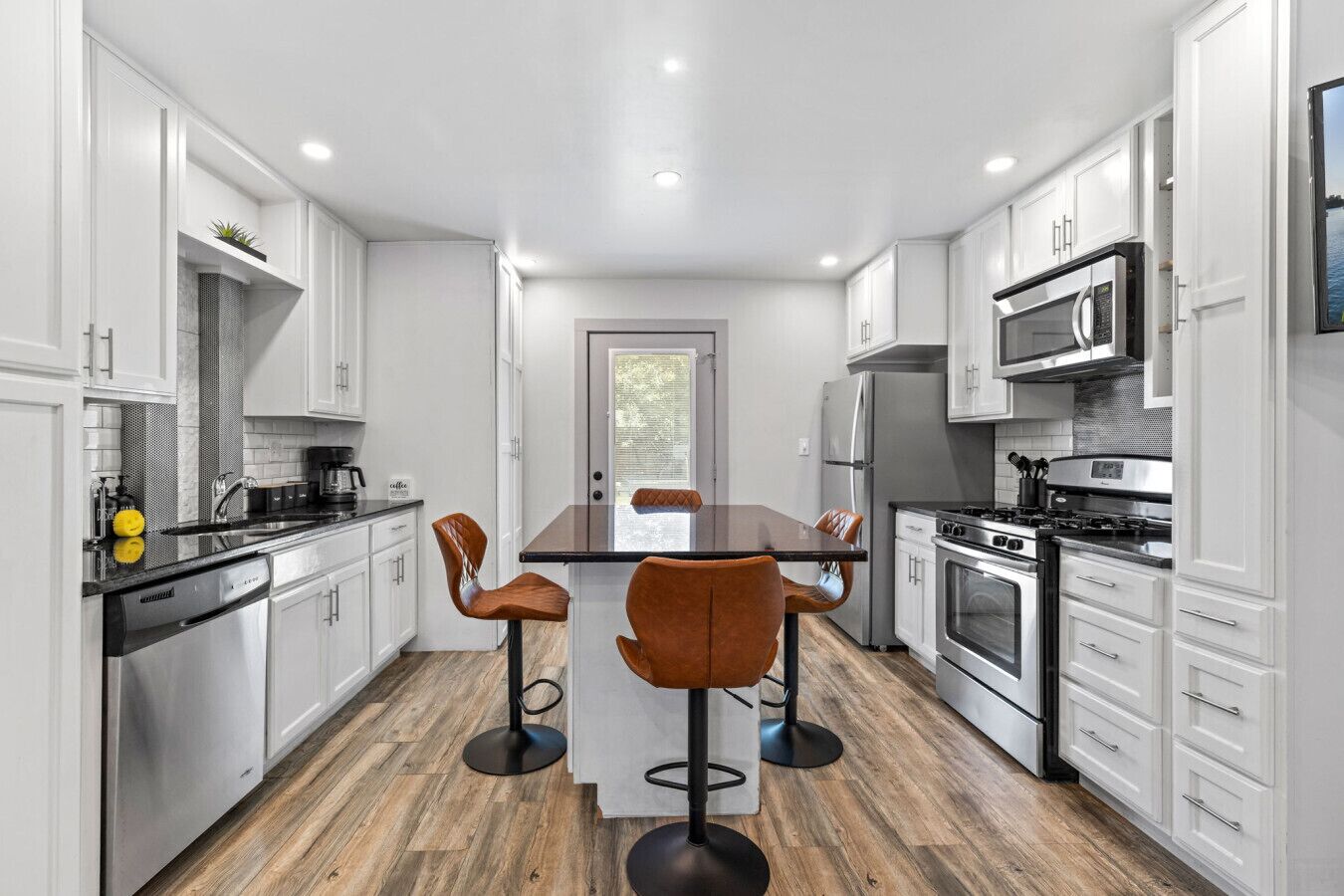 A modern kitchen with white cabinetry, a central island with stools, stainless steel appliances, and a wooden floor.