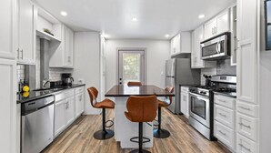 A modern kitchen with white cabinetry, a central island with stools, stainless steel appliances, and a wooden floor.