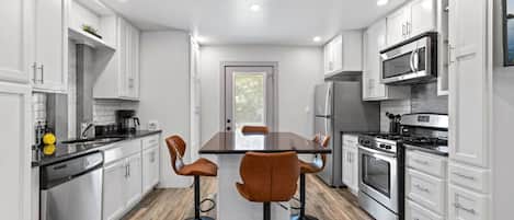 A modern kitchen with white cabinetry, a central island with stools, stainless steel appliances, and a wooden floor.
