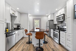 A modern kitchen with white cabinetry, a central island with stools, stainless steel appliances, and a wooden floor.
