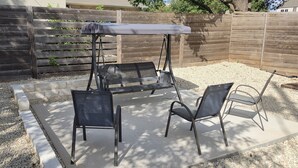 A patio area with a swing set, two chairs, and a table with a canopy.