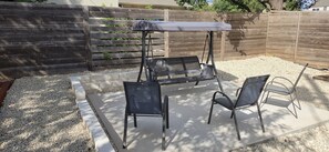 A patio area with a swing set, two chairs, and a table with a canopy.