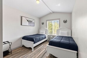 Une chambre avec deux lits, une fenêtre avec des stores, un luminaire au plafond et une œuvre d’art accrochée au mur.