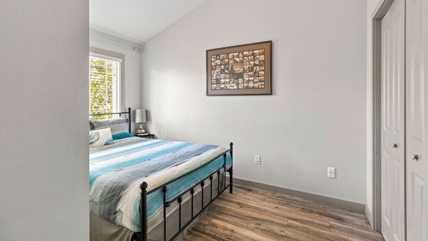A bedroom with a bed, a nightstand, a lamp, a framed picture on the wall, and a wooden floor.