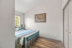 Une chambre à coucher avec un lit, une table de chevet, une lampe, un tableau encadré au mur et un plancher en bois.