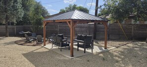 A covered outdoor seating area with a wooden structure, surrounded by gravel, and adjacent to a wooden fence. - Spectacular Austin SoCo Townhome (Austin)