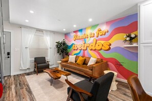 A modern living room with a colorful mural, a brown leather sofa, a wooden coffee table, and a grey armchair. - Retro SoCo GetawayTownhome! (Austin)