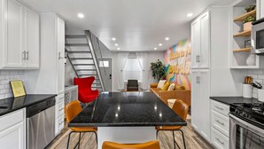 A modern kitchen with white cabinets, a black countertop, and a central island with orange chairs. - Retro SoCo GetawayTownhome! (Austin)