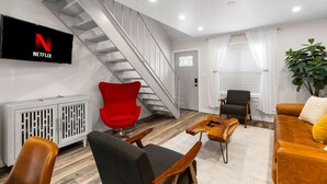 A modern living room with a staircase, a red chair, a sofa, and a TV displaying the Netflix logo. - Retro SoCo GetawayTownhome! (Austin)