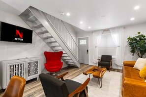 A modern living room with a staircase, a red chair, a sofa, and a TV displaying the Netflix logo. - Retro SoCo GetawayTownhome! (Austin)