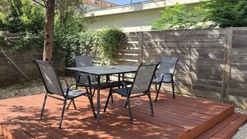 Une terrasse avec une table et quatre chaises, entourée d’une plateforme en bois et d’une clôture en bois.