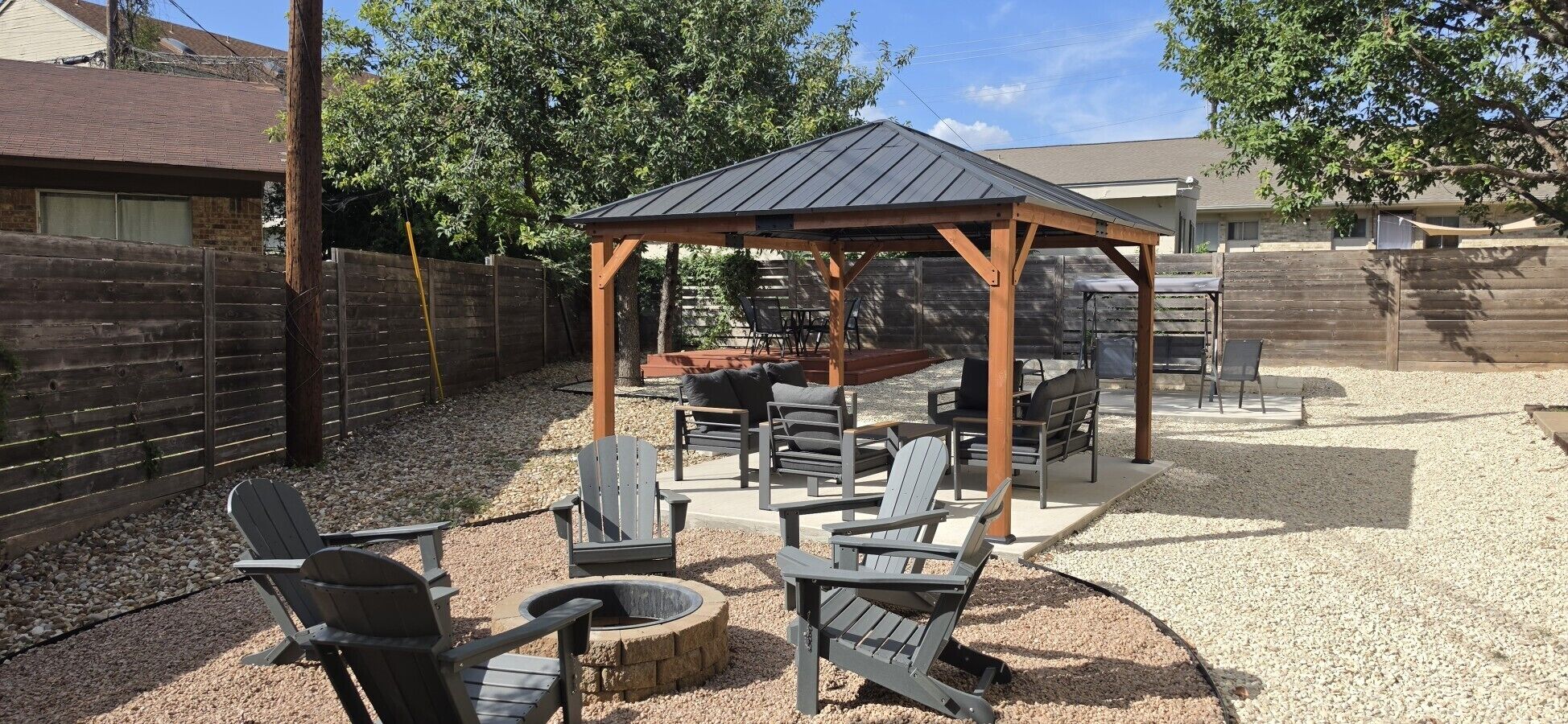 Un'area patio esterna con una pergola in legno, zone salotto e un braciere.