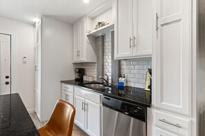 A modern kitchen with white cabinetry, stainless steel appliances, and a black countertop. - Retro SoCo GetawayTownhome! (Austin)